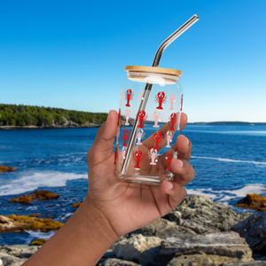 Hand holding glass with lobster design in front of ocean with rocks