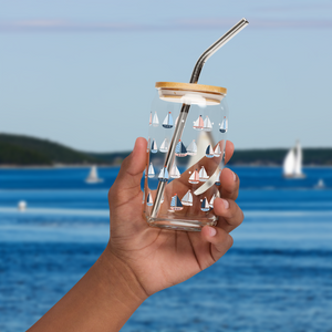 Hand holding an empty glass with a sailboat design in front of an ocean background